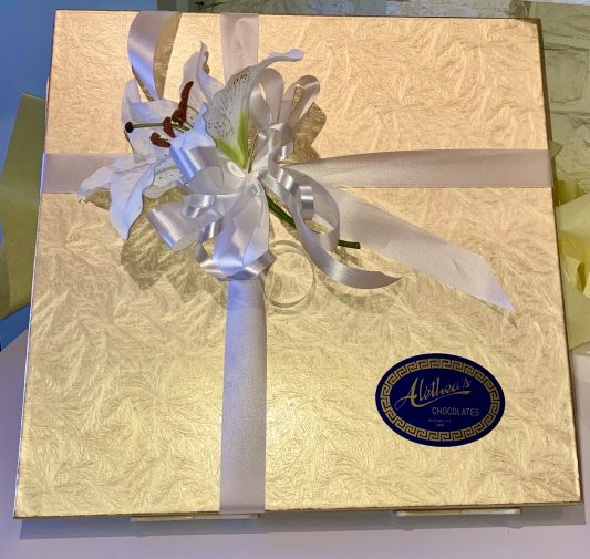 gold box of gourmet chocolates decorated with white lilies for Mothers day